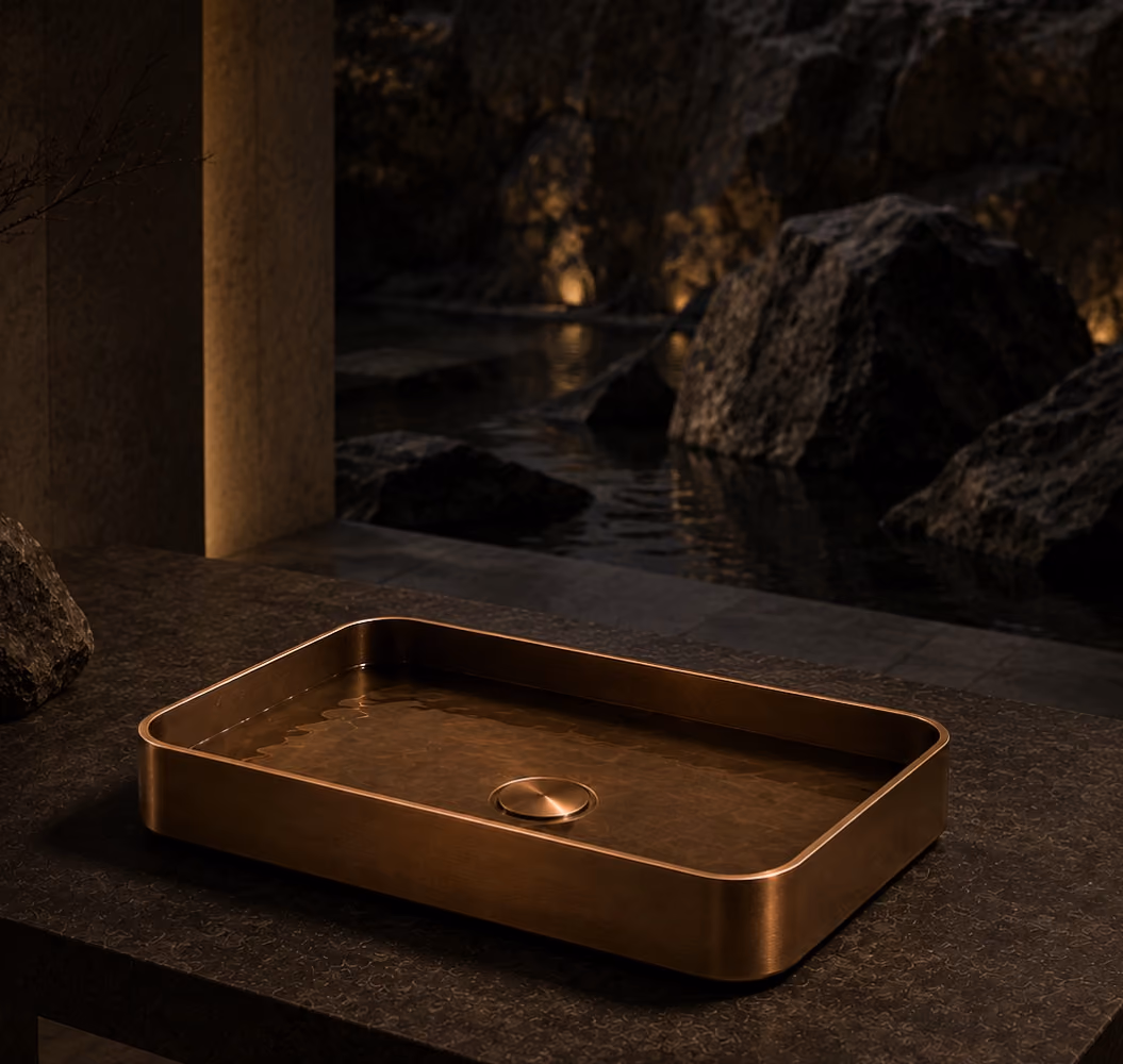 Inox bronze rectangular countertop wash basin on a dark stone ledge with a lit rocky pool behind