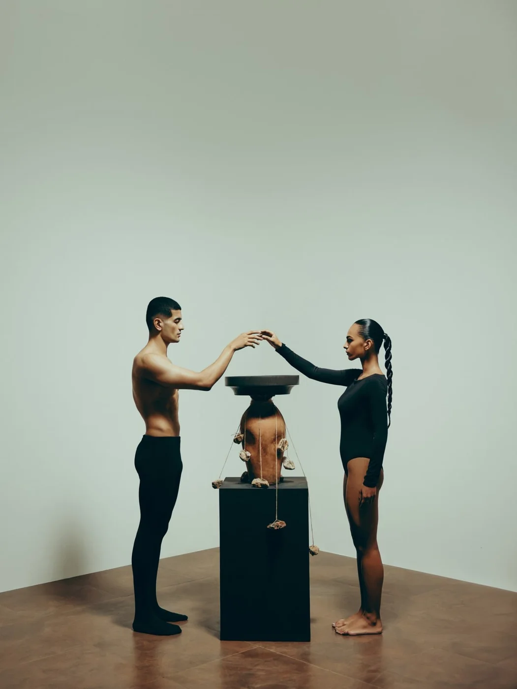 Two models reaching over a sculptural terracotta basin on a black plinth — Ode to Germany campaign